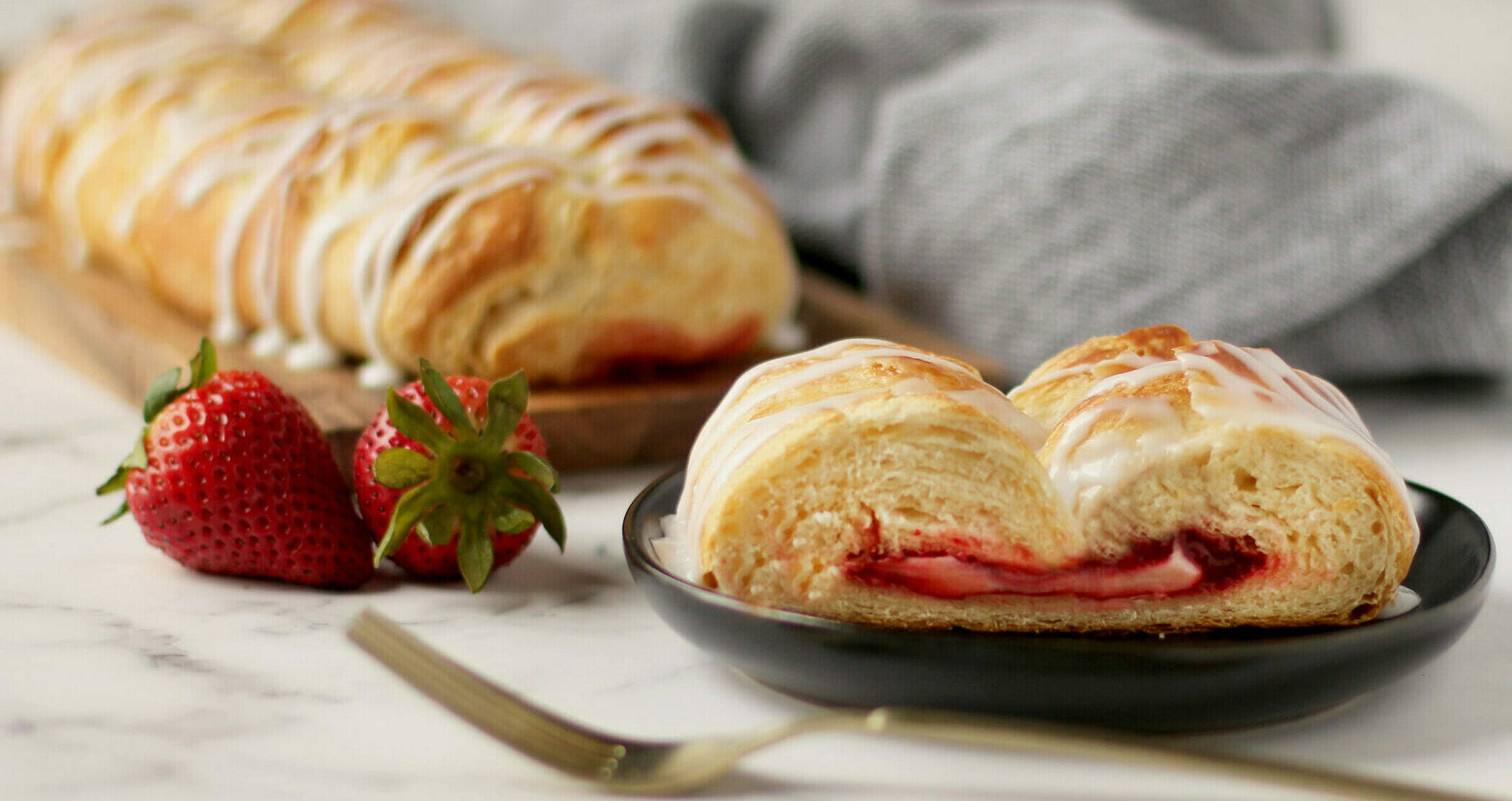 Strawberry Cream Cheese Pastry with icing in the background. A slice of pastry on a plate with fork and strawberries.